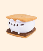 Left quarter view of s’mores-inspired plush. This view shows Pusheen’s white marshmallow feet extending off her body resting atop the chocolate slab.  