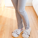 Model wearing the Pusheen Plush Slippers, wearing loose grey pajama pants and standing on top of a wooden floor.