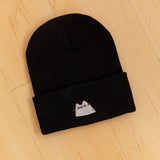 Top view of black knit hat laid on a light yellow hardwood surface.