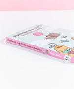 The Pusheen book lying on top of white surface to show off the pink book spine with Pusheen floating using a balloon.