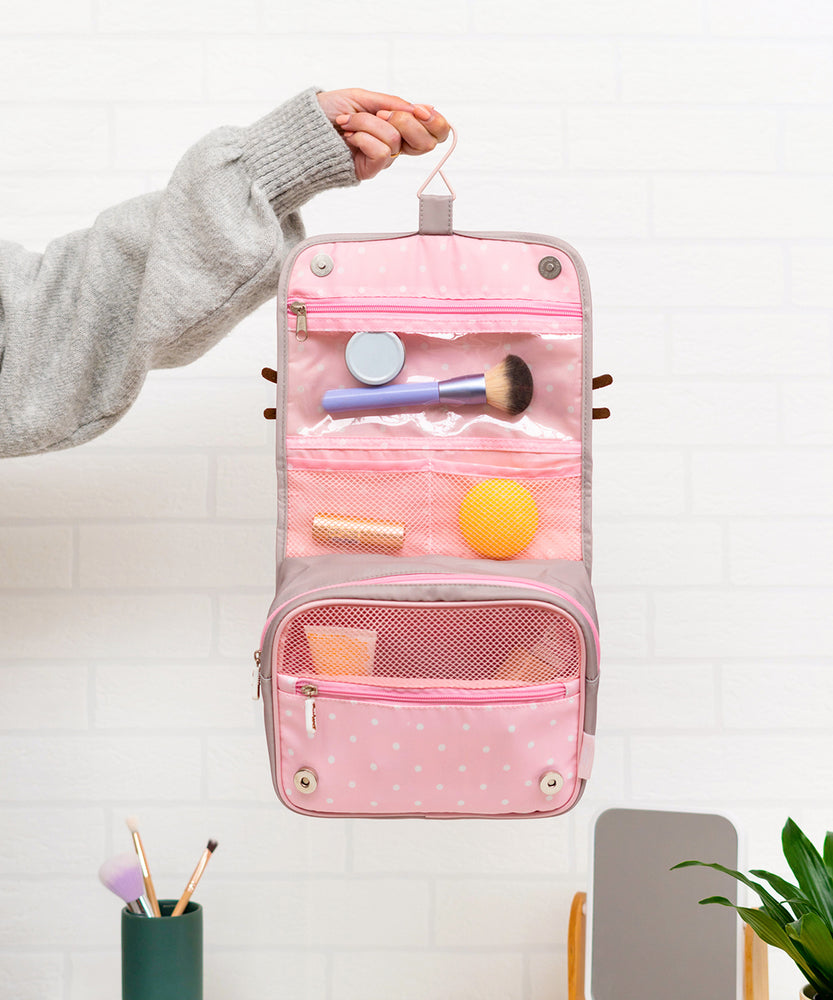 Back view of the grey toiletry bag. The back has a storage slot. Below the storage slot is a saying “Bon Meowage” in white and pink print. The “O” in Bon is a two-toned pink glazed donut.  