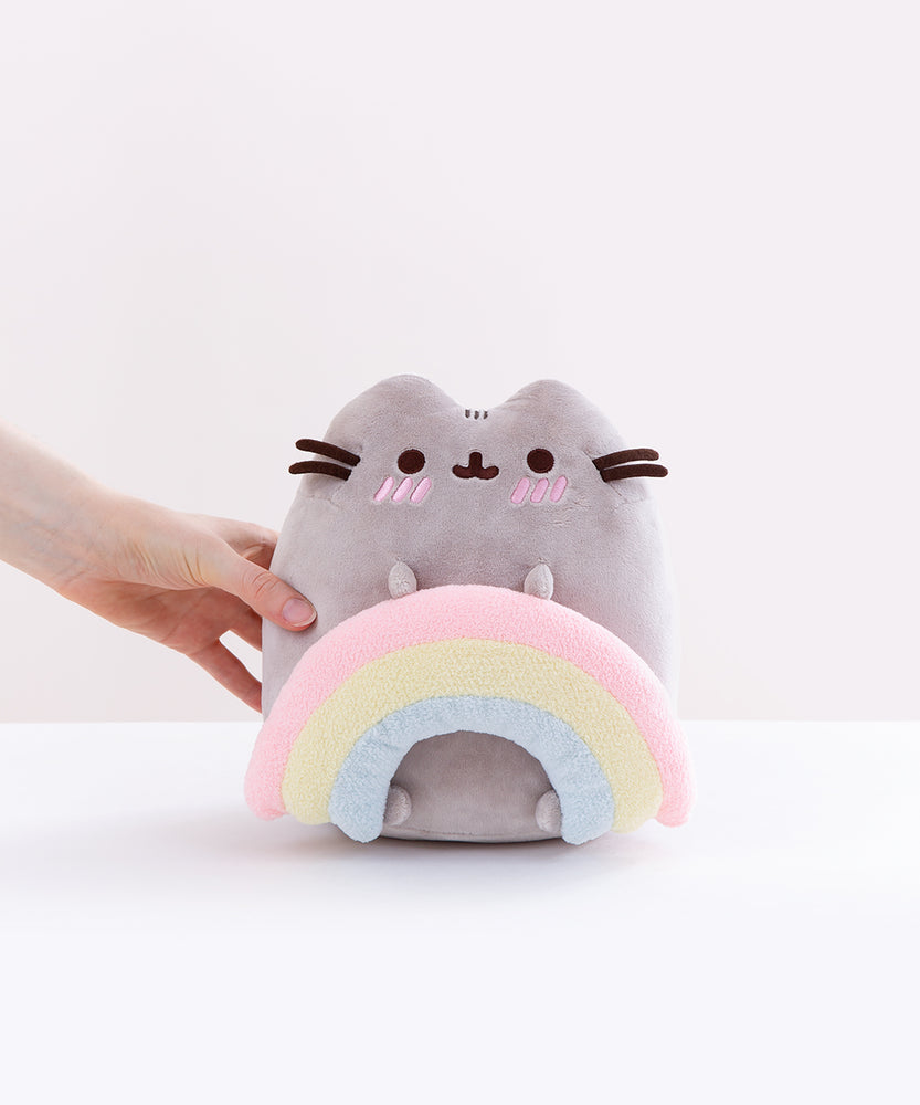 Model’s hand loosely holding the Pusheen with Rainbow Plush in front of a white background.