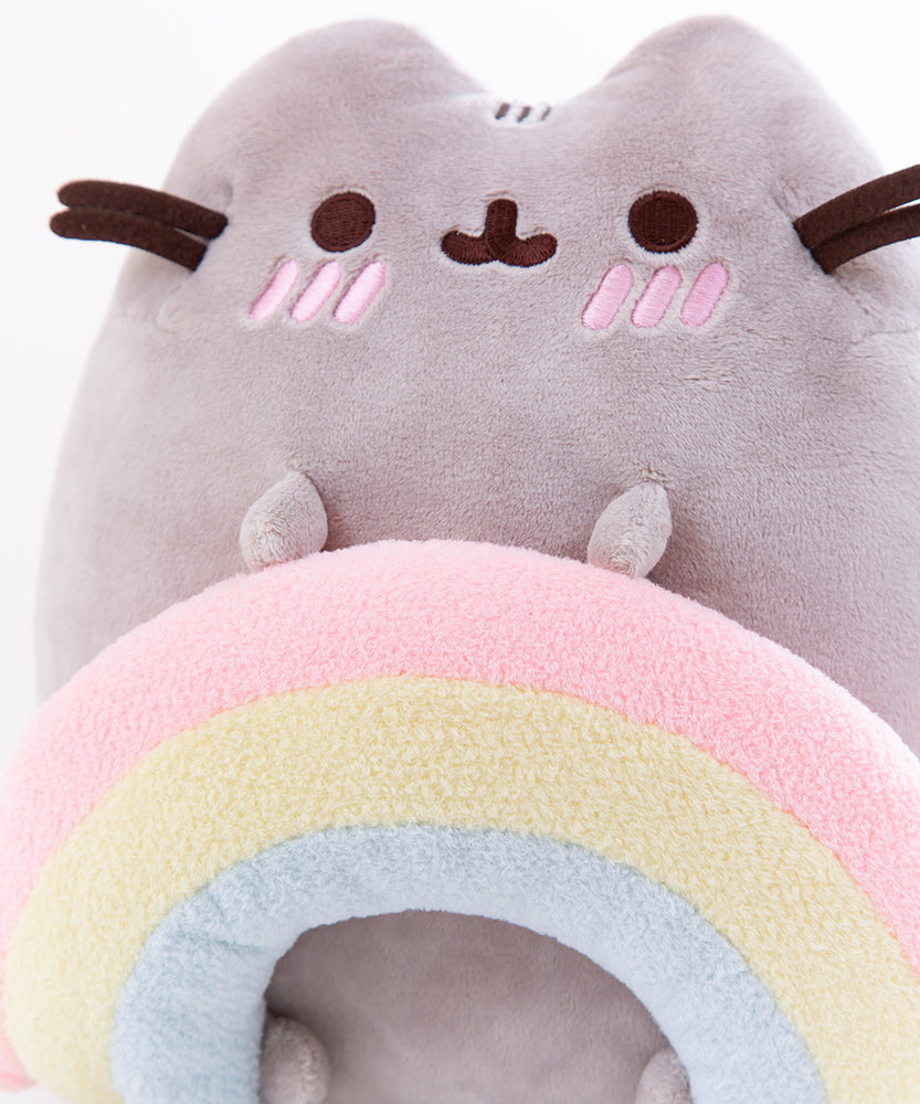 Back view of the Pushen with Rainbow Plush in front of a white background. Pusheen’s back has the standard two back stripes and a striped tail. Pusheen’s whiskers and rainbow stick out partially from the other side. The information tag for the plush is located to the left of the tail.