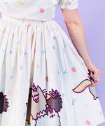 Closeup view if printed Pusheenicorn pattern skirt pattern. White skirt is dotted with pastel pink, purple, blue and yellow magical jewels with a repeating border pattern of Pusheenicorn carrying a pink cupcake in her mouth while walking alongside her and friends. 