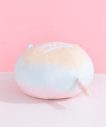 The back quarter view of the Rainbow Ombre Round Squisheen Plush sitting on top a white surface. Pusheen the Cat’s tail is striped light yellow and pastel pink striped. 
