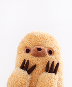 Close up of Sloth’s face peeking up from the bottom, hands to his face. Sloth’s snout is a darker brown and a smoother fabric then the rest of his fur. His nose is embroidered in dark brown directly on his snout. His snout is placed directly in between his eyes, which are dark brown embroidered dots with a light brown embroidered circle around them. Sloth’s claws are plush made with a felt-like fabric