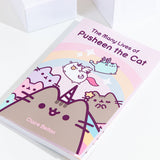 The Many Lives of Pusheen the Cat book resting at an angle on top of a white background, with white cubes above the book. 