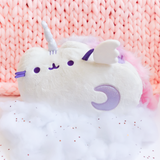 The Super Musical Pusheenicorn Plush couched in the cotton ball clouds, dotted with shiny silver star confetti. The plush is in front of a large piece of pink knit fabric.