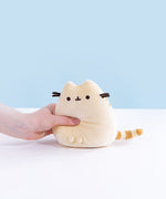 A model’s hand squeezing the Yellow Mini Squisheen Plush, demonstrating it’s squishiness.