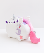 Quarter view of the Super Pusheenicorn Musical Plush facing the left in front of a white background. Super Pushenicorn’s mane starts behind her horn, goes behind her right ear, and runs straight down her back through the  two back stripes. It ends close to her tail. There is a white plush wing on each side of the mane. The plush tag is right bright the tail.