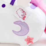 Close up of the light purple sparkly crescent moon embroidered into the plush. There is a lenticular hangtag hanging from the wing featuring Super Pusheenicorn flapping her wings. Underneath the moon is a paper star hangtag reading ‘Press for lights and sound!’