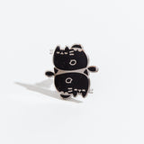 The Pisces pin on a white background. The pin feature two Pusheens with closed eyes and fish fins, mirroring each other vertically. The pin is black with multicolor sparkles and a silver outline.