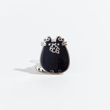 The Virgo pin on a white background. The pin features Pusheen with a leaf laurel, chewing on a flower in her paws. The pin is black with multicolor sparkles and a silver outline.